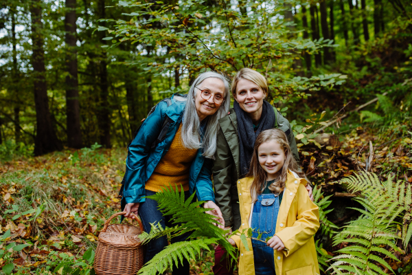 A small girl with mother and grandmother on walk outoors in forest, looking at camera.