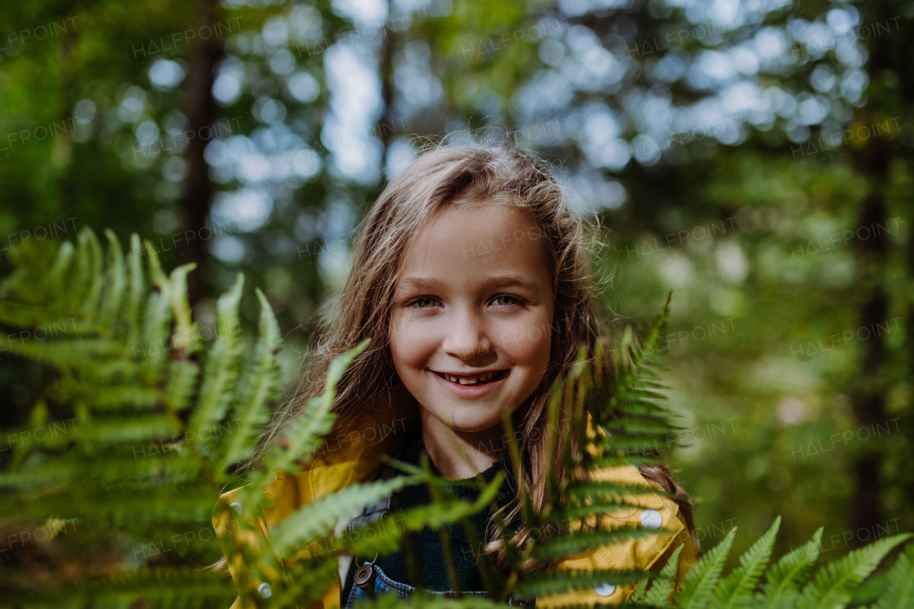 A happy little girl holding fern and looking at camera outdoors in forest.