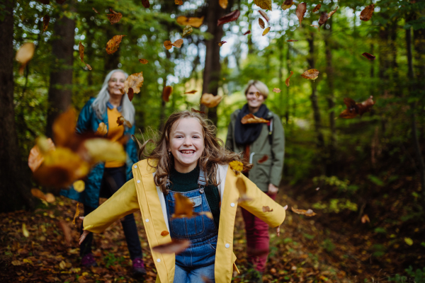 A happy little girl with basket running during walk with mother and grandmother outdoors in forest