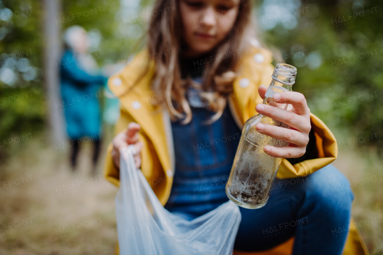 Close-up of a small girl picking up waste in plastic bag outoors in forest, during autumn day.