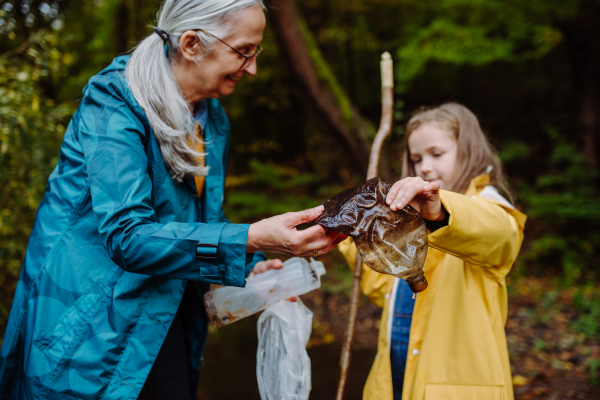 A small girl with grandmother showing plastic waste what they found outoors in forest.