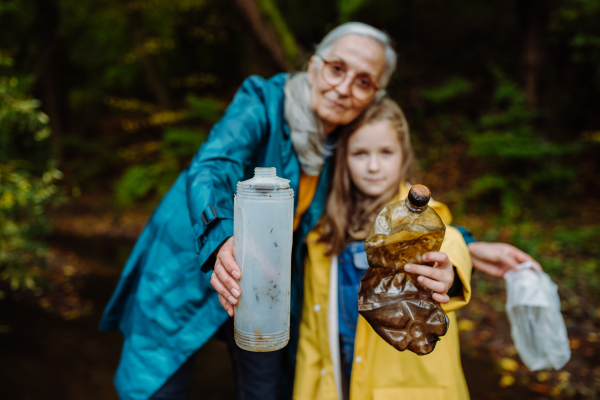 A small girl with grandmother showing plastic waste what they found outoors in forest.