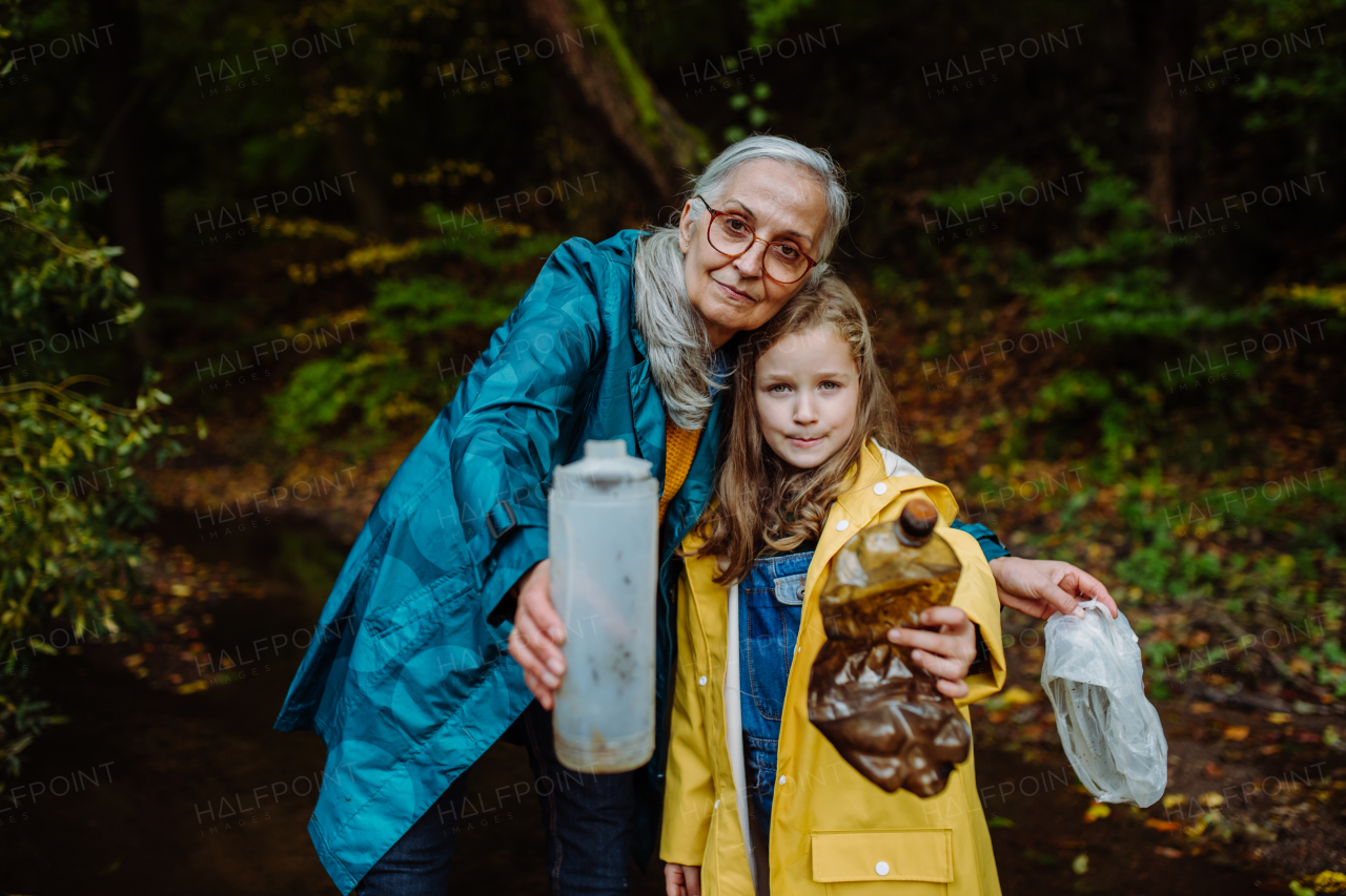 A small girl with grandmother showing plastic waste what they found outoors in forest.