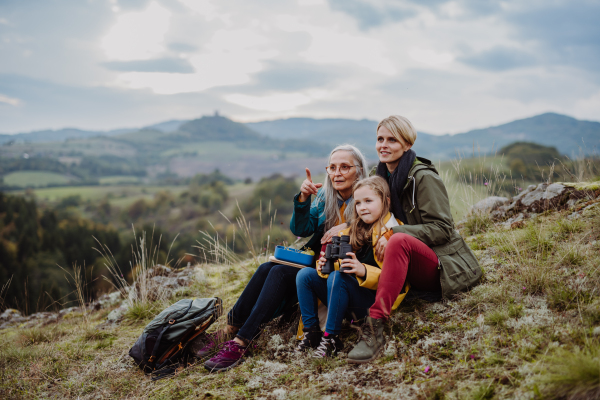 A small girl with mother and grandmother sitting and lookiong at view on top of mountain.