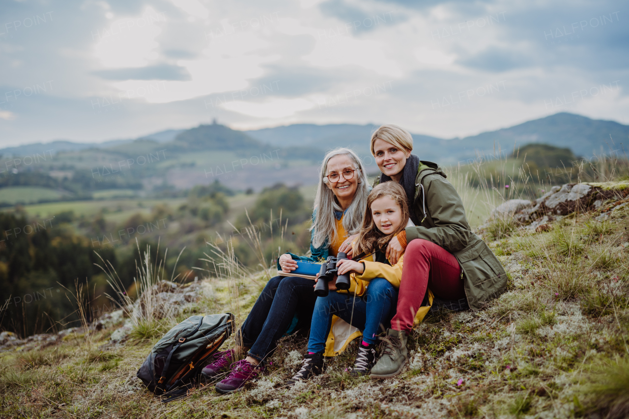 A small girl with mother and grandmother sitting and lookiong at camera on top of mountain.