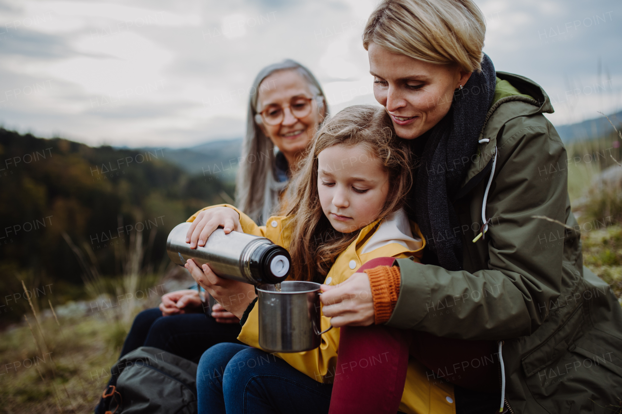 A small girl with mother and grandmother sitting and pouring hot tea on top of mountain.