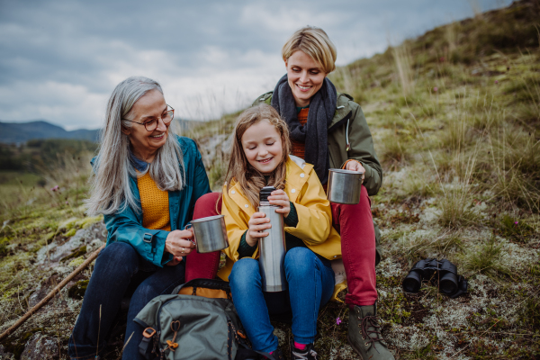 A small girl with mother and grandmother sitting and drinking hot tea on top of mountain.