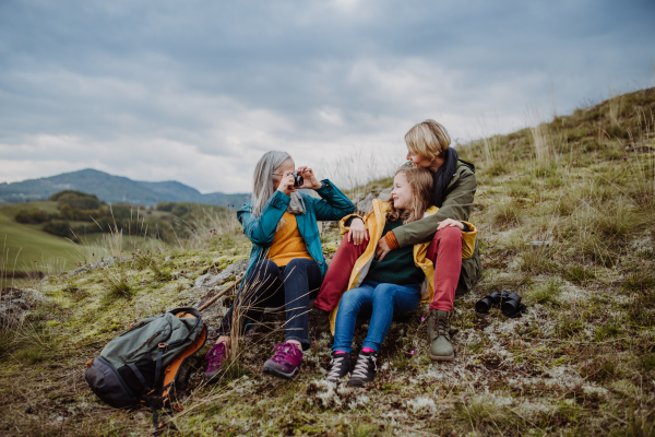 A senior woman taking picture of her daughter and granddaughter on top of hill in autumn day.