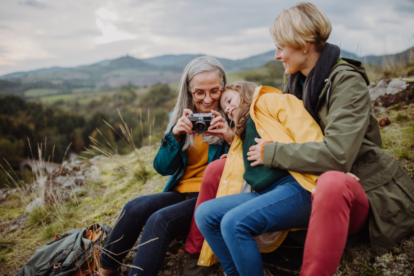 A senior woman taking picture of her daughter and granddaughter on top of hill in autumn day.