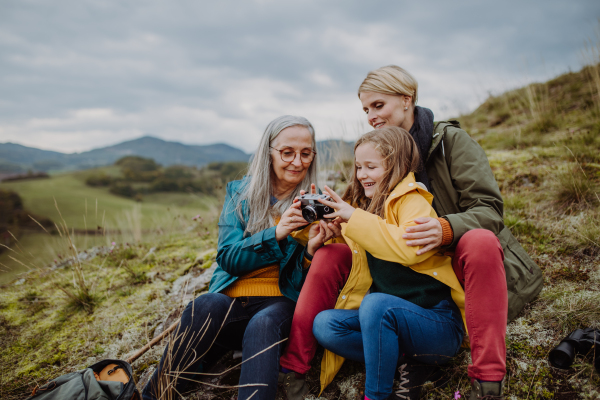 A senior woman taking picture of her daughter and granddaughter on top of hill in autumn day.