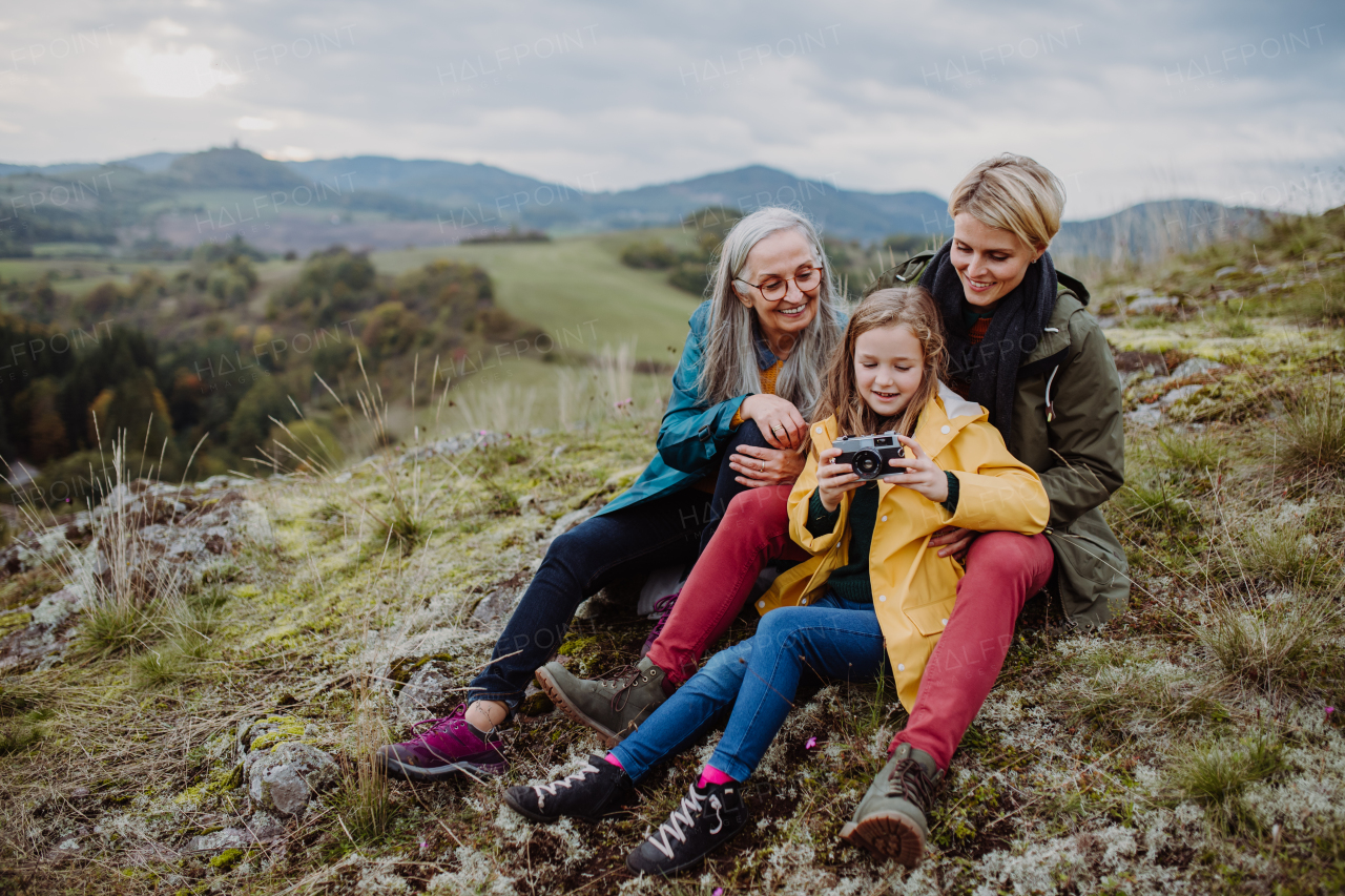 A senior woman taking picture of her daughter and granddaughter on top of hill in autumn day.