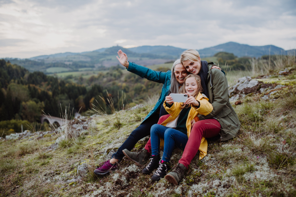 A small girl with mother and grandmother taking selfie outoors on top of mountain.