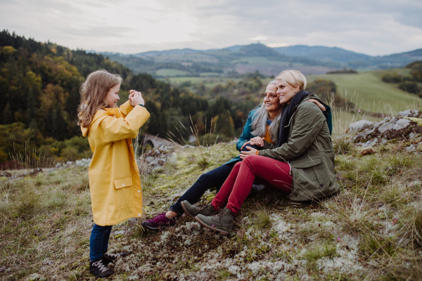 A small girl with mother and grandmother taking photography outoors on top of mountain.