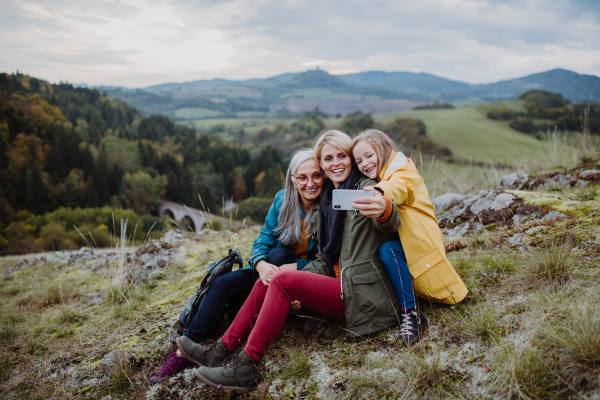 A small girl with mother and grandmother taking selfie outoors on top of mountain.