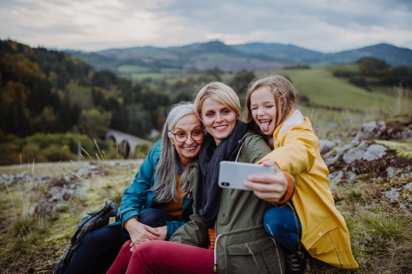 A small girl with mother and grandmother taking selfie outoors on top of mountain.