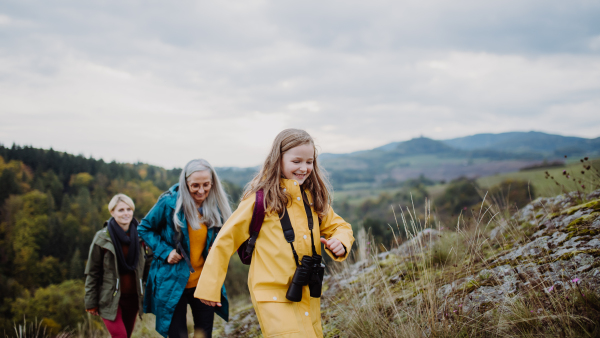 A portrait of small girl with mother and grandmother standing and looking at camera outoors in nature.