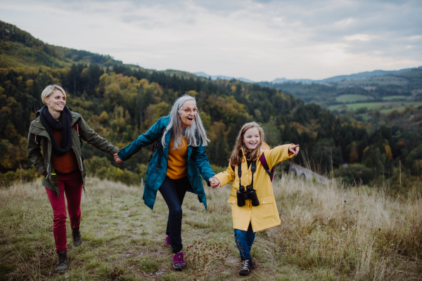 A portrait of small girl with mother and grandmother standing and looking at camera outoors in nature.