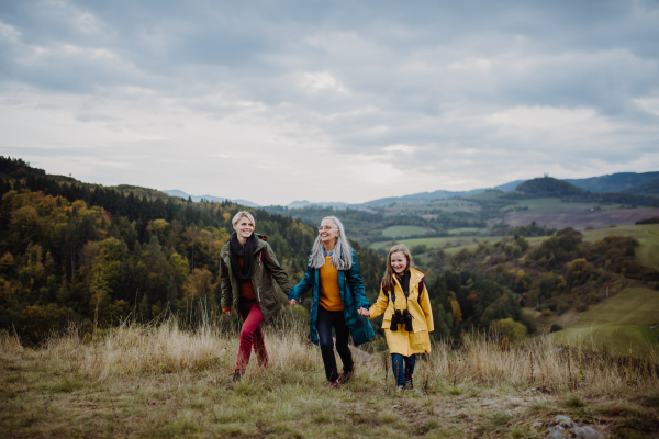 A portrait of small girl with mother and grandmother standing and looking at camera outoors in nature.