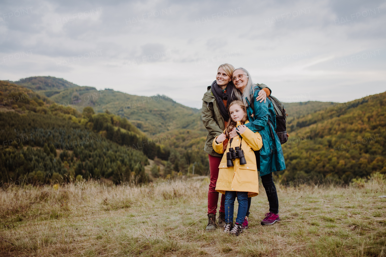 A small girl with mother and grandmother standing and lookiong at view on top of mountain.