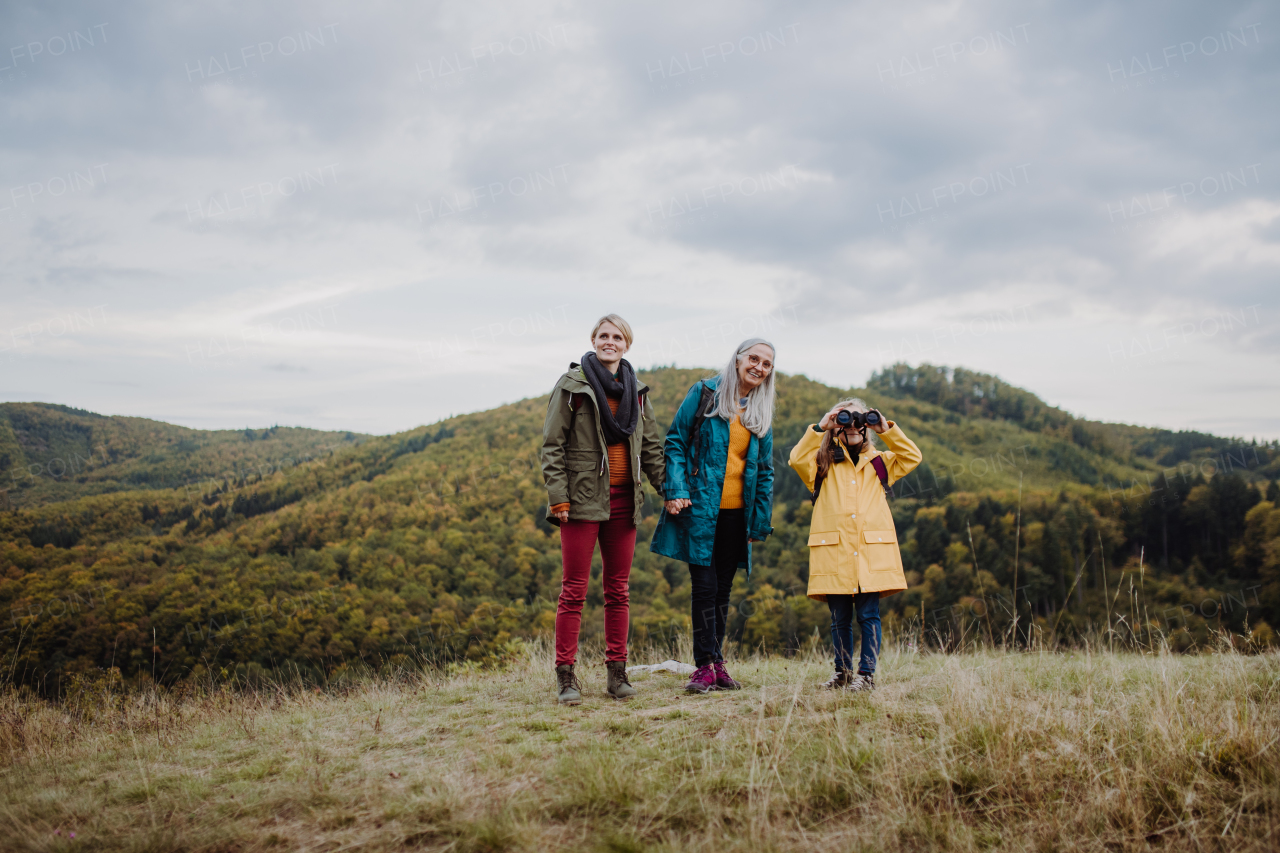 A small girl with mother and grandmother hiking outoors in autumn nature.