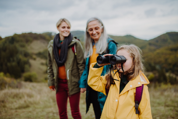 A portrait of small girl with mother and grandmother standing and looking at camera outoors in nature.