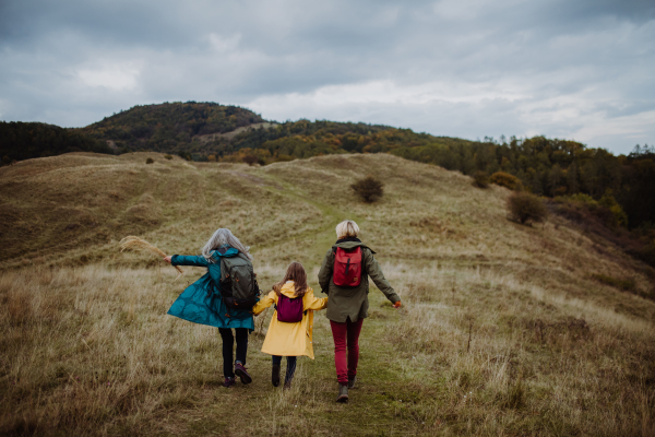 A rear view of small girl with mother and grandmother hiking outoors in autumn nature.