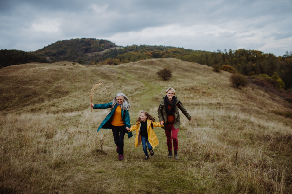 A small girl with mother and grandmother hiking outoors in autumn nature.