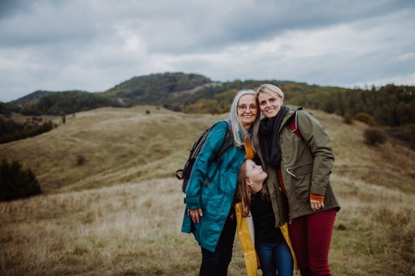 A portrait of small girl with mother and grandmother standing and looking at camera outoors in nature.