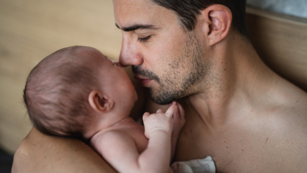 A close up of father holding and kissing his newborn baby indoors at home