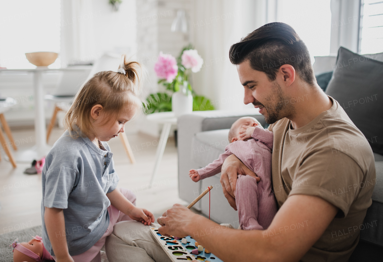 A happy young man taking care of his newborn baby and little daughter indoors at home, paternity leave.