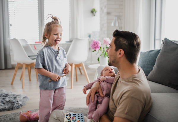 A happy young man taking care of his newborn baby and little daughter indoors at home, paternity leave.