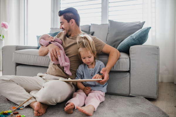 A happy young man taking care of his newborn baby and little daughter indoors at home, paternity leave.