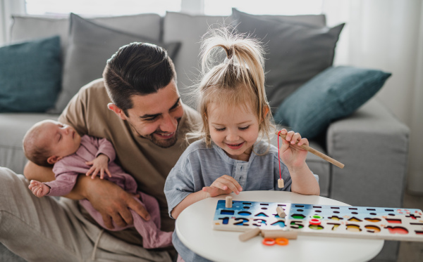 A happy young man taking care of his newborn baby and little daughter indoors at home, paternity leave.