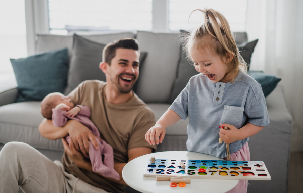 A happy young man taking care of his newborn baby and little daughter indoors at home, paternity leave.