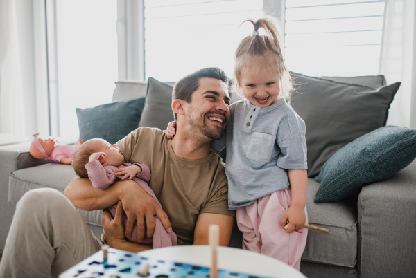 A happy young man taking care of his newborn baby and little daughter indoors at home, paternity leave.