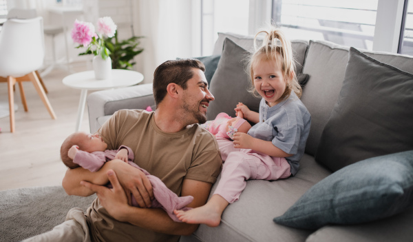 A happy young man taking care of his newborn baby and little daughter indoors at home, paternity leave.