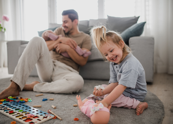 A happy young man taking care of his newborn baby and little daughter indoors at home, paternity leave.