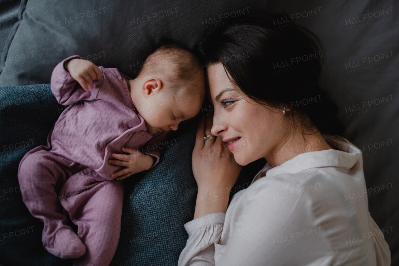 A top view of happy young mother with her newborn baby girl lying on sofa indoors at home.