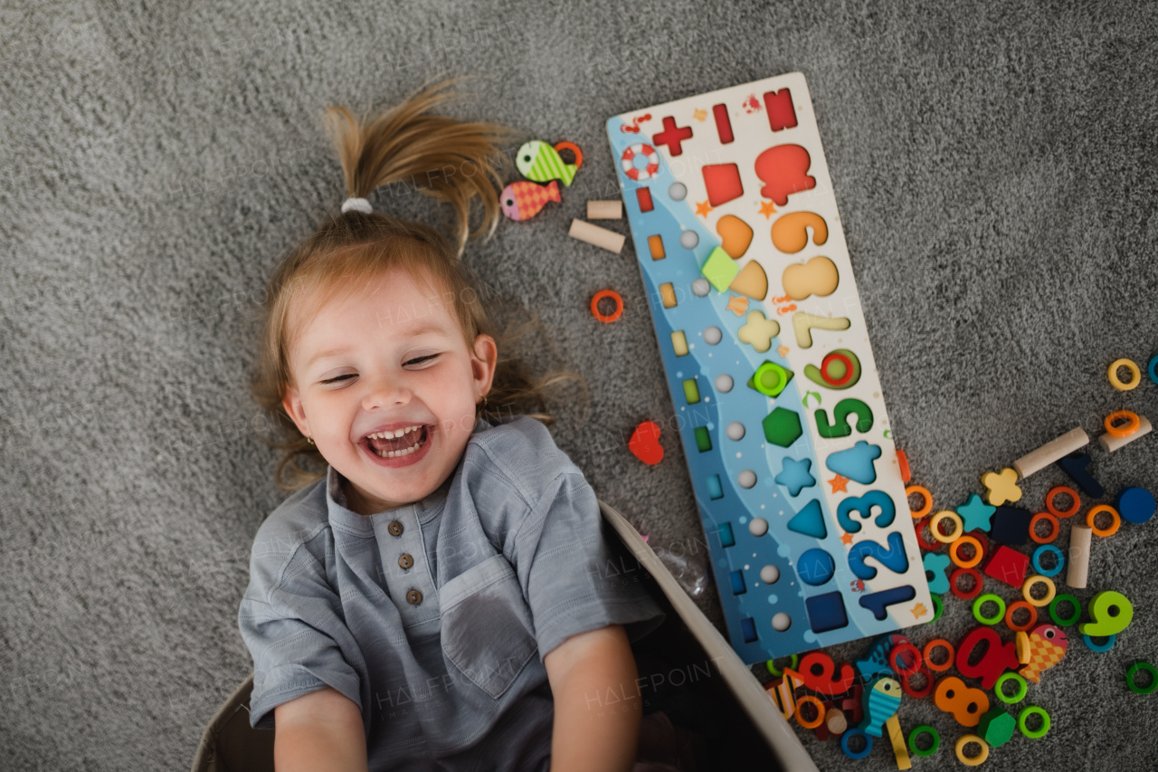 A top view of little cauccasian girl lying on floor laughing indoors at home.