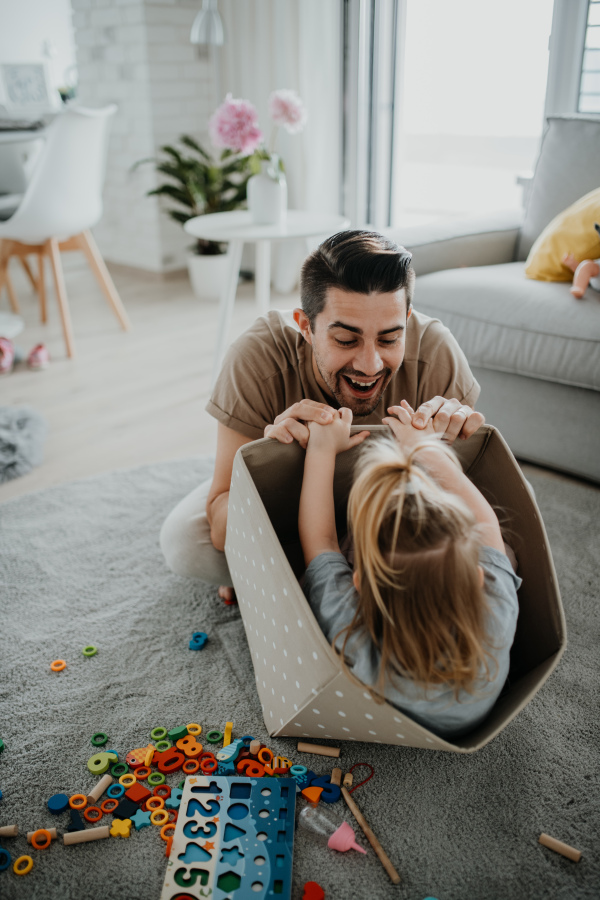 A happy young father with little daughter playing and having fun together at home.