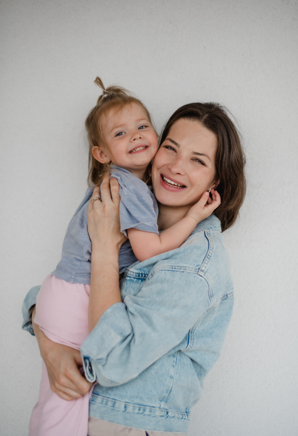 A portrait of happy young mother with her little daughter hugging and looking at camera, on white background.