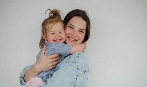 A portrait of happy young mother with her little daughter hugging and looking at camera, on white background.