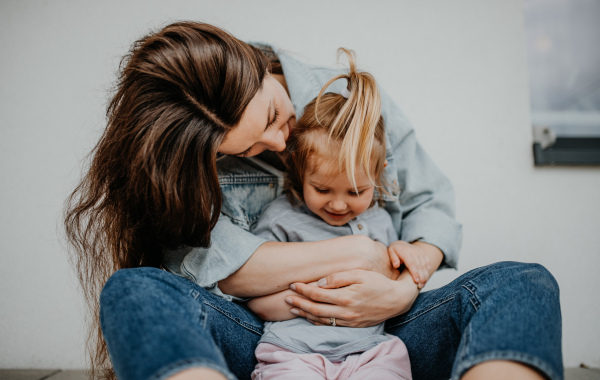 A portrait of happy young mother with her little daughter hugging on white background.