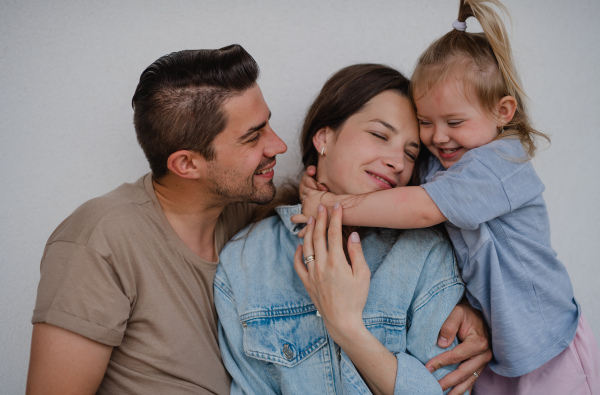 Portrait of happy young parents with a little daughter hugging on white background.