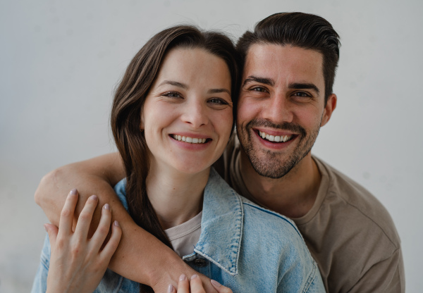 A portrait od happy young couple hugging and looking at camera, on white background.