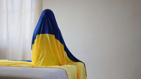 An unrecognizable person sitting, covered with Ukrainian flag, unity with Ukraine concept.