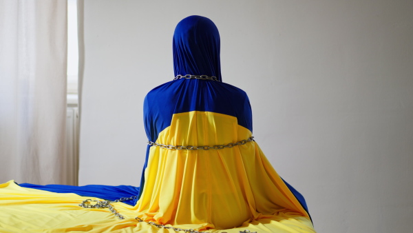 A rear view of unrecognizable person covered with flag, bounded with chains, Ukrainian flag concept.