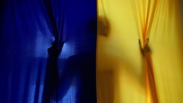 A silhouette of woman behind yellow and blue Ukrainian flag.