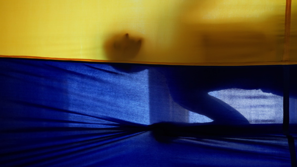 A silhouette of woman behind yellow and blue Ukrainian flag.