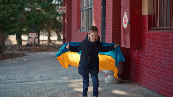 A boy holding Ukrainian flag and running in train station.